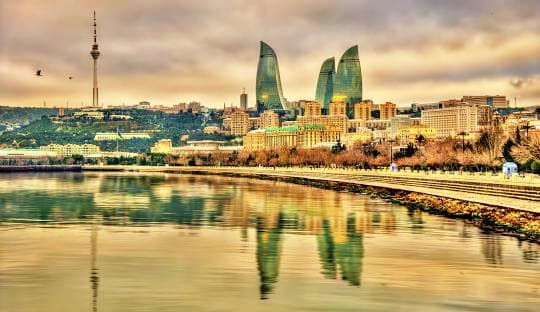 Baku skyline with Flame Towers reflected in Caspian Sea, TV tower and waterfront buildings at sunset